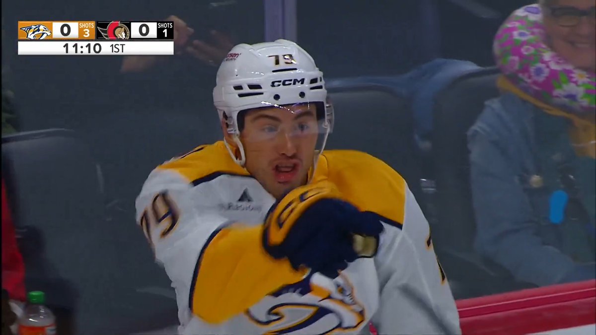 Nashville Predators player #79, wearing a white and yellow jersey and CCM helmet, is shown during a scoreless first-period game against the Ottawa Senators (scoreboard reads 0-0 with 11:10 remaining in the 1st, Predators with 3 shots and Senators with 1). The image relates to the caption as #79 is likely Ross Colton, who scored his first goal with the Predators in this matchup.