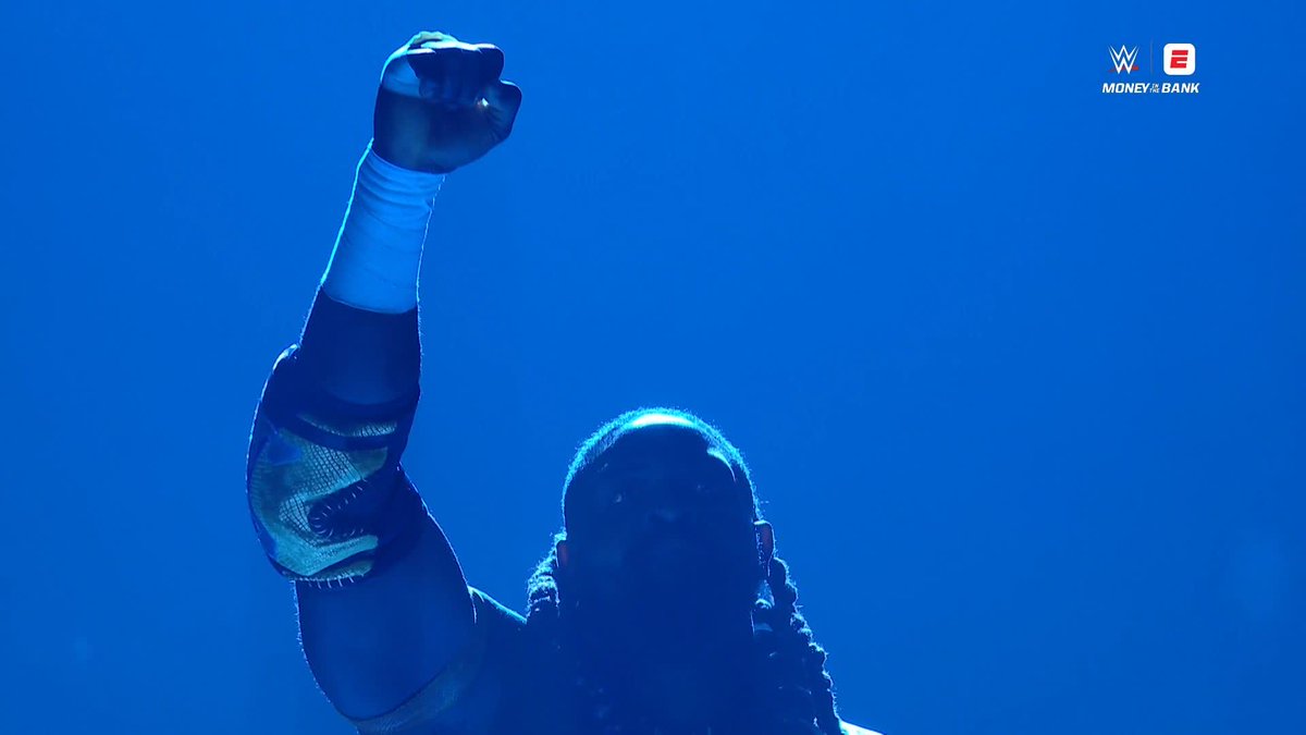 A bearded wrestler stands silhouetted against a dramatic blue backdrop with his right arm raised triumphantly, fist clenched, while wearing a wristband and elbow pad. The image features a "WWE MONEY IN THE BANK" logo in the upper right corner, accompanying the caption "THE RULER IS HERE" referencing @Obaofwwe.