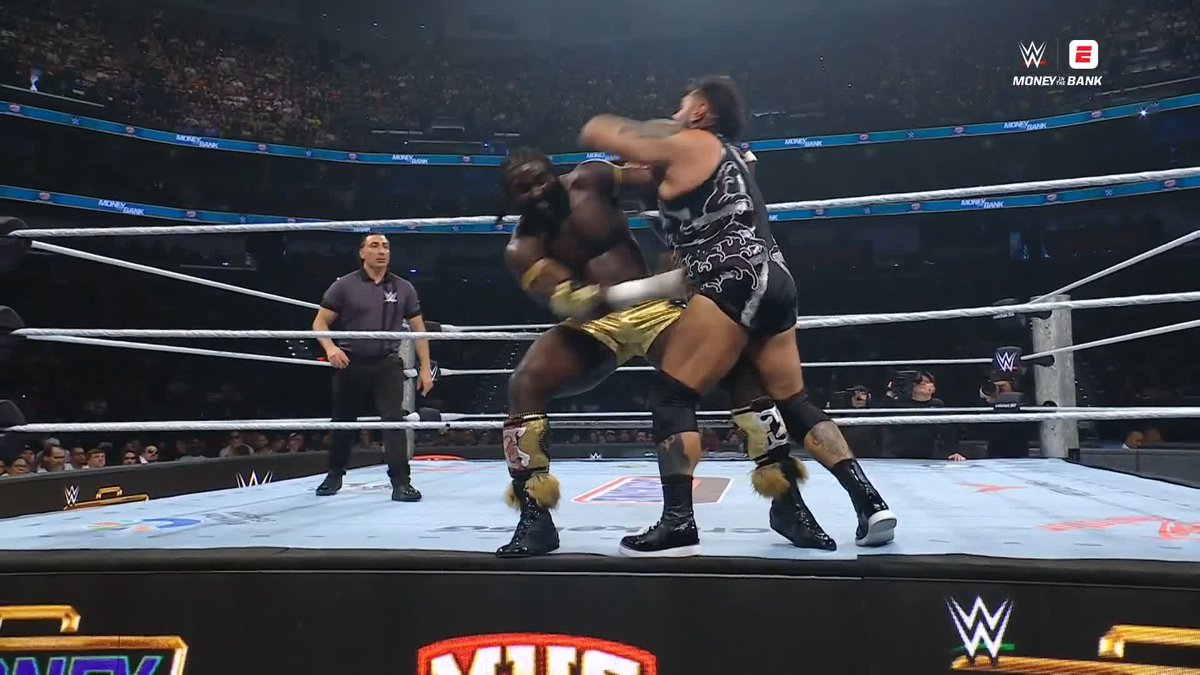 Two WWE wrestlers are locked in a fierce grappling exchange in the center of the ring during a Money in the Bank event, with the referee closely monitoring the action as one wrestler grabs his opponent by the neck. The intense physicality shown in the image perfectly matches the caption's description of Bronson Reed's (@BRONSONISHERE) match being "PHYSICAL early."
