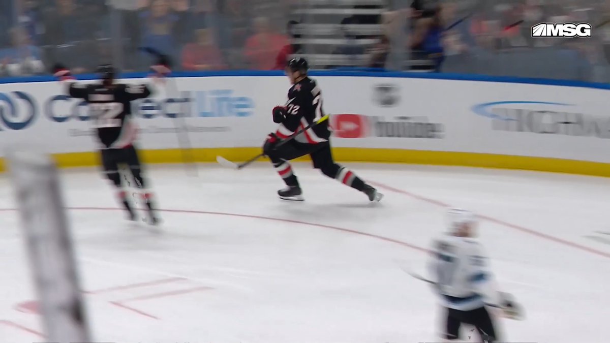 A blurry screenshot from an MSG hockey broadcast shows players in action on the ice, with a player in a dark #12 jersey and Coors Lite and YouTube advertisements on the boards.