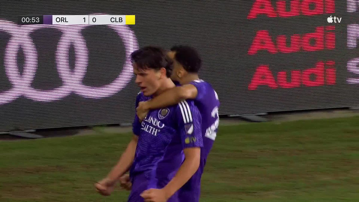 Two Orlando City soccer players in purple "Orlando Health" jerseys celebrate on the field during a match against CLB, with the scoreboard reading ORL 1 - 0 CLB at 00:53.