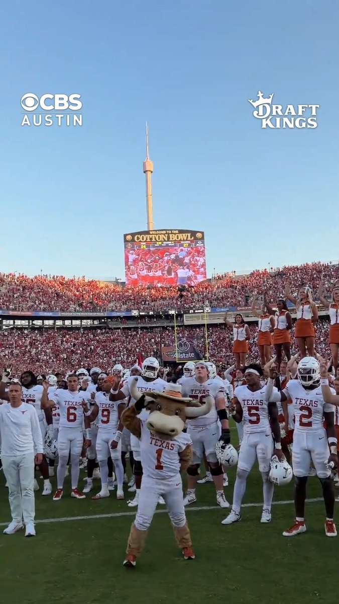 Texas Longhorns football team celebrating on the field at the Cotton Bowl, with their mascot Bevo (wearing jersey #1) in front and cheerleaders behind, sponsored by CBS and DraftKings.