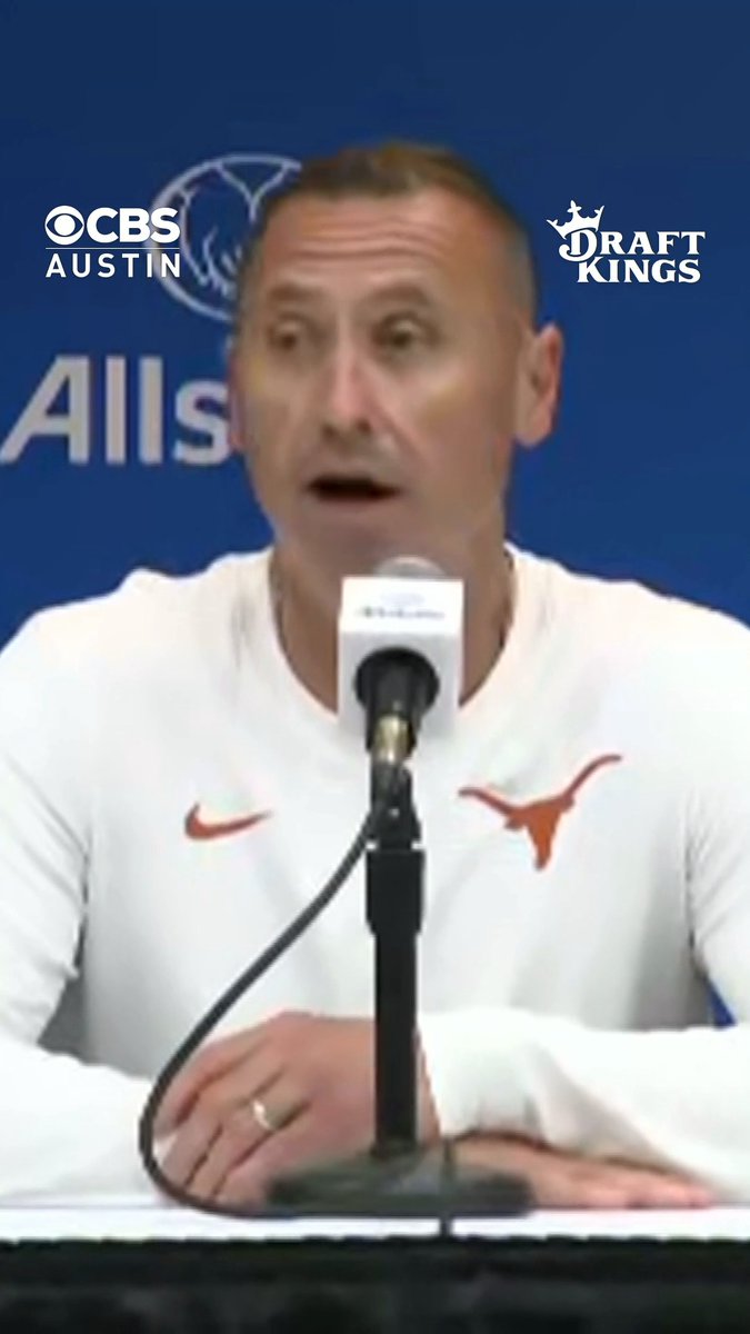 A man in a white Texas Longhorns shirt speaks at a press conference microphone, with CBS Austin and DraftKings logos visible.