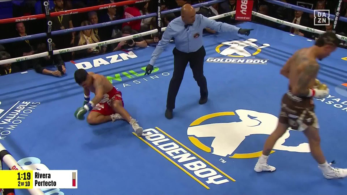 A knockdown occurs in the ring at 1:19 of Round 2, with the on-screen graphic identifying the fighters as Rivera and Perfecto. The referee gestures toward Rivera, who stands upright, while Perfecto sits on the canvas following a knockdown, matching the caption of Rivera dropping Perfecto in the 2nd round during a DAZN broadcast.