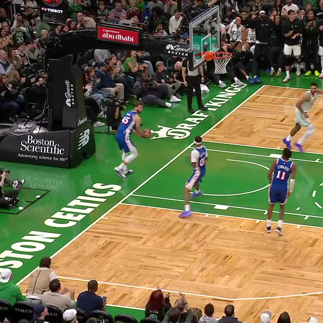 An NBA game is in progress at Boston's TD Garden, where the home team Celtics are playing against a team in blue uniforms, with visible signage including "Boston Scientific," "DraftKings," and "Experience Abu Dhabi." Players wearing jerseys with numbers 11 and 45 are positioned on the court near the hoop.