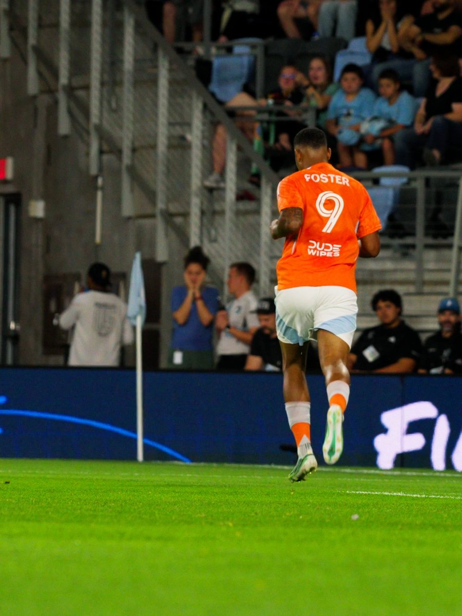 A soccer player wearing an orange jersey with 'FOSTER' and the number 9, along with 'Dude Wipes' sponsor, runs on the field during a match.