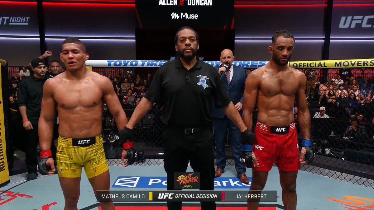 A referee raises the hands of UFC competitors Matheus Camilo and Jai Herbert following their official decision match at UFC Fight Night, with Herbert wearing red shorts and victorious according to the post's claim of his back-to-back win.