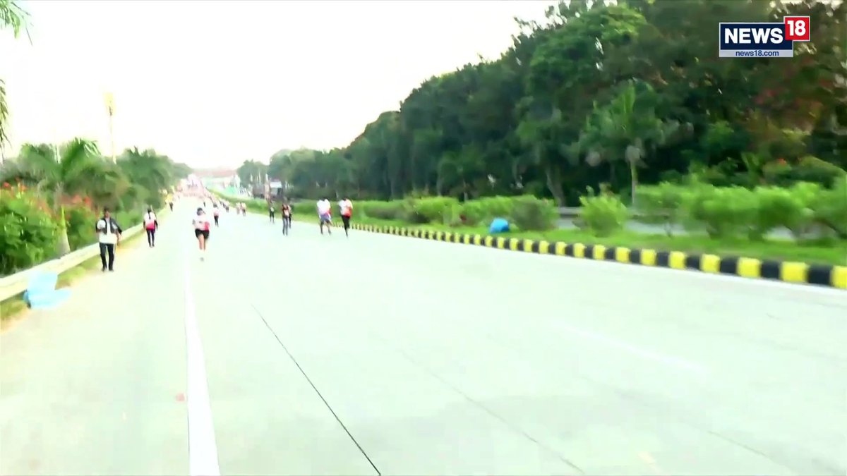 Runners participate in the Namma Run Bengaluru 2026 along a tree-lined road, with the News18 logo displayed in the corner, supporting a drug-free fitness initiative that drew over 10,000 participants.