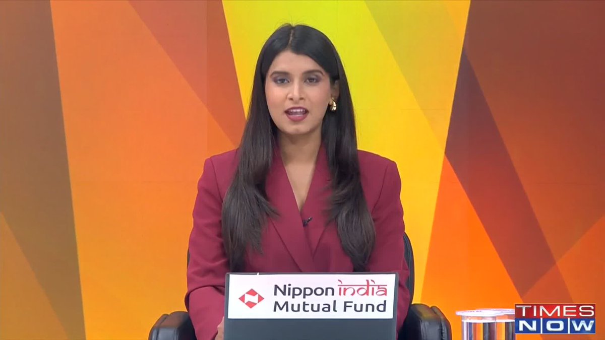 News anchor Kritika Tiwari sits at a desk featuring "Nippon India Mutual Fund" branding on a Times Now broadcast, with the channel's logo visible in the corner against a vibrant orange and yellow geometric backdrop.
