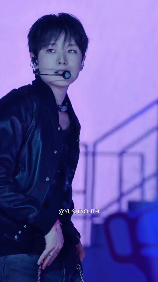 A performer on stage wearing a black leather jacket and headset microphone, lit with purple lighting, with the watermark '@YUSHIYOUTH'.