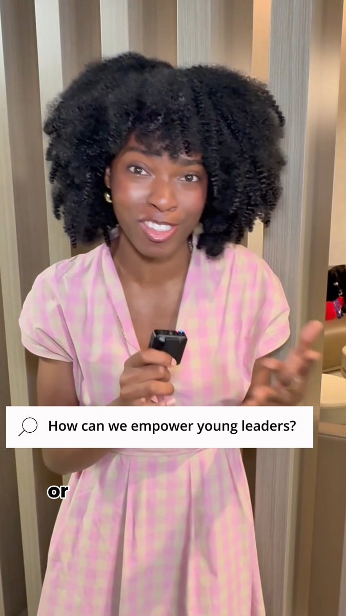 Still from a video featuring a young woman with curly hair in a pink patterned dress holding a small microphone, with an on-screen question box reading 'How can we empower young leaders?'