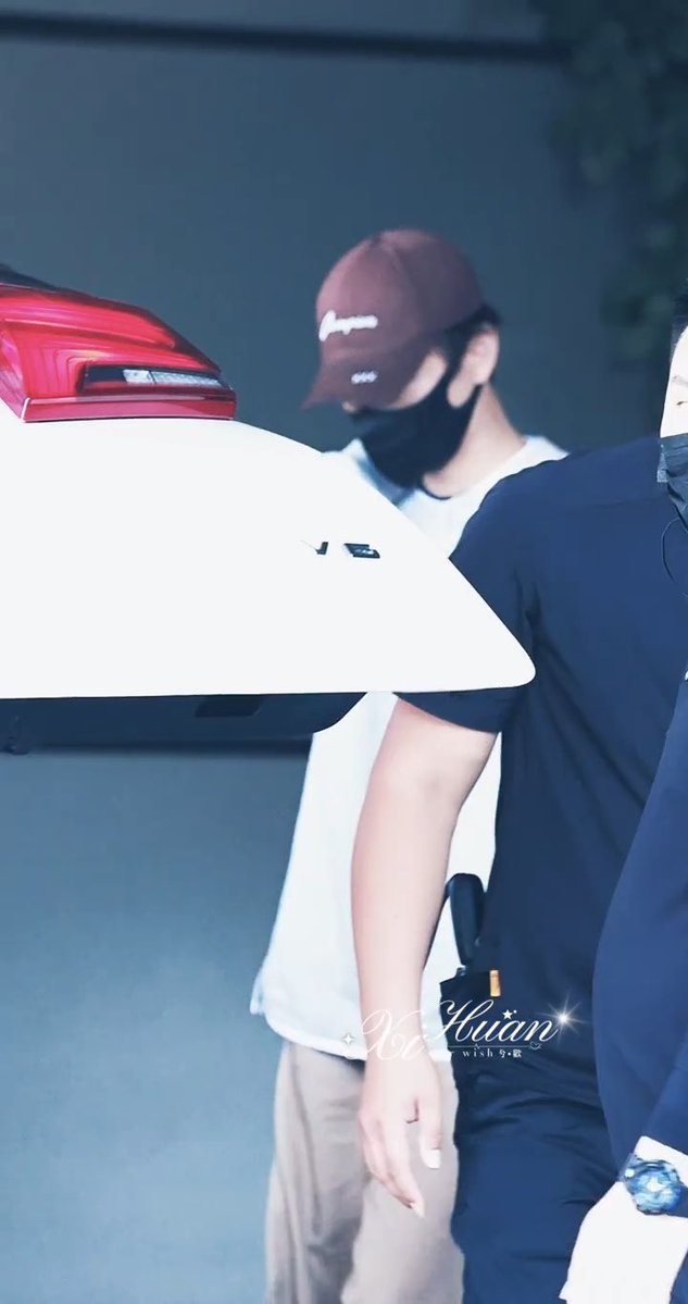 A blurry photograph of a person wearing a maroon Champion cap and black face mask standing near a white car, with a watermark reading "Xu Huân wish 夕歡" visible on the image.