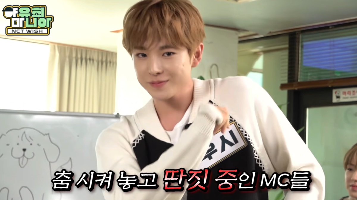 A young man with light brown hair smiles at the camera in what appears to be a variety show setting, with Korean text '춤시커 놓고 단직 증인MC를' and '우리동네 NCT WISH' logo visible on screen.