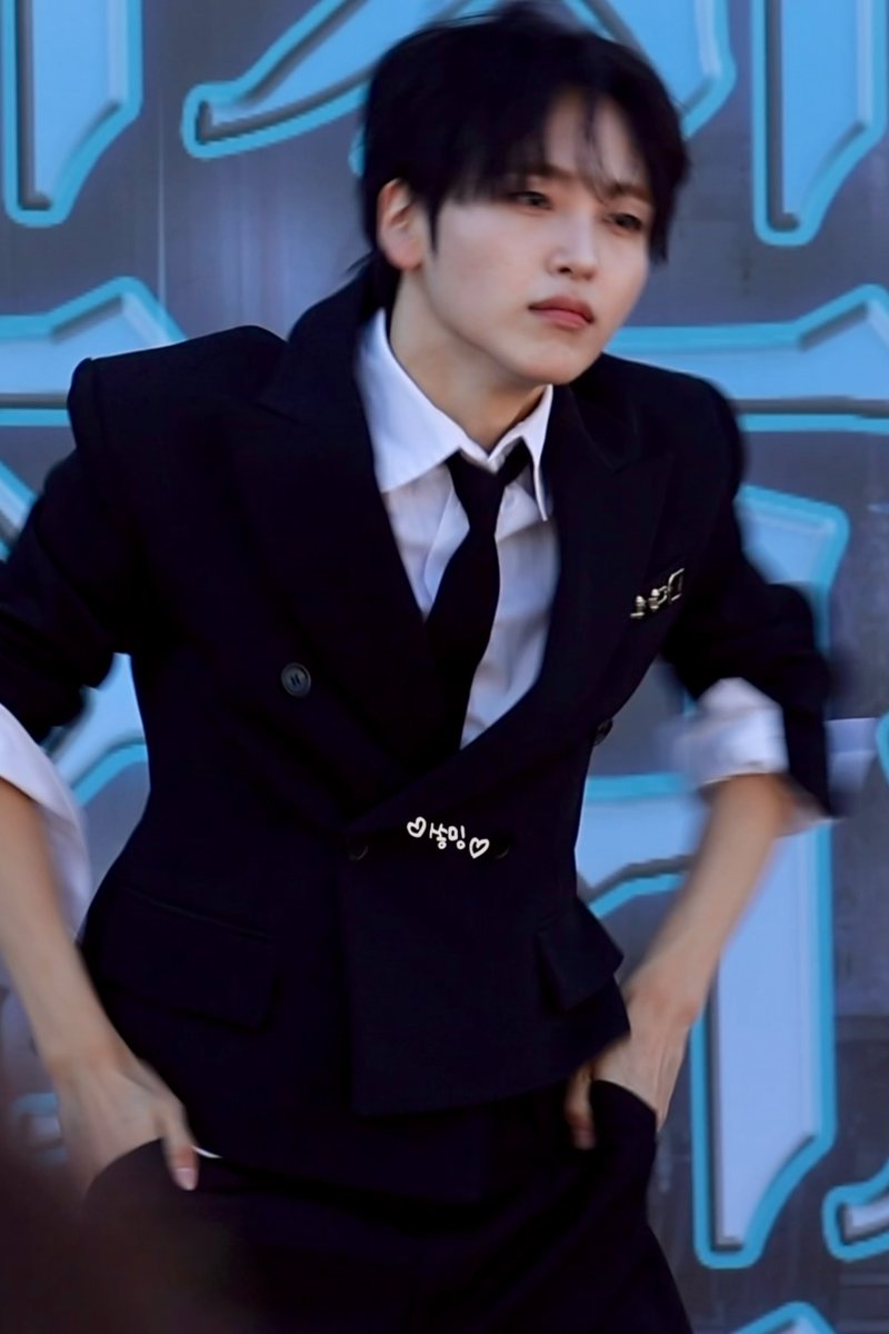 A young man in a black double-breasted suit and tie poses against a blue illuminated background, with Korean text '넘어' visible on the image.
