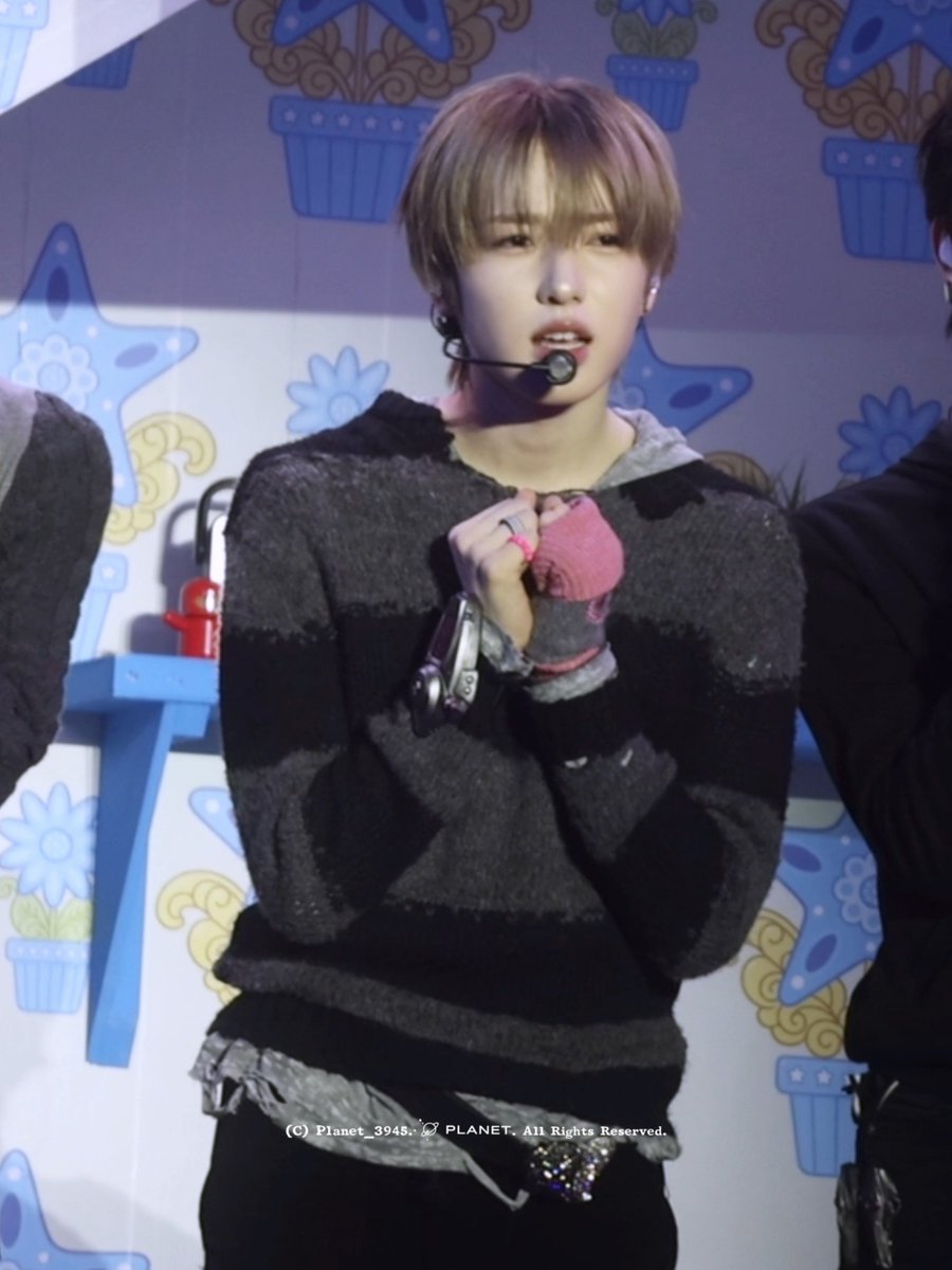 A young performer with reddish-brown hair wears a headset microphone and a striped sweater with a pink fingerless glove, appearing to be in the middle of a song with an expressive face on stage. The image is watermarked "(C) Planet_3945. PLANET. All Rights Reserved." and relates to a showcase post featuring NCT WISH member Sakuya, as indicated by the hashtags #Sakuya #SAKUYA #サクヤ #NCTWISH and the "Facial Expression Control No. 1" caption.