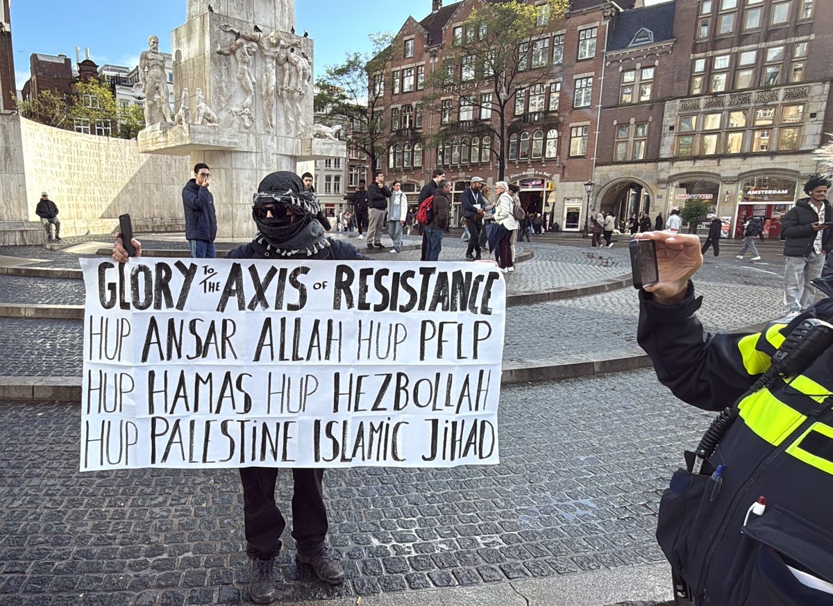 EppoTjuchem's tweet photo. "GLORY TO THE AXIS OF RESISTANCE: ... HUP HAMAS, HUP HEZBOLLAH ...." 

Recht voor ons Nationaal Monument - de plek waar we slachtoffers van terreur herdenken - staat men ongestoord terreur toe te juichen.

En de politie? Die staat er naast en maakt er rustig foto's van.