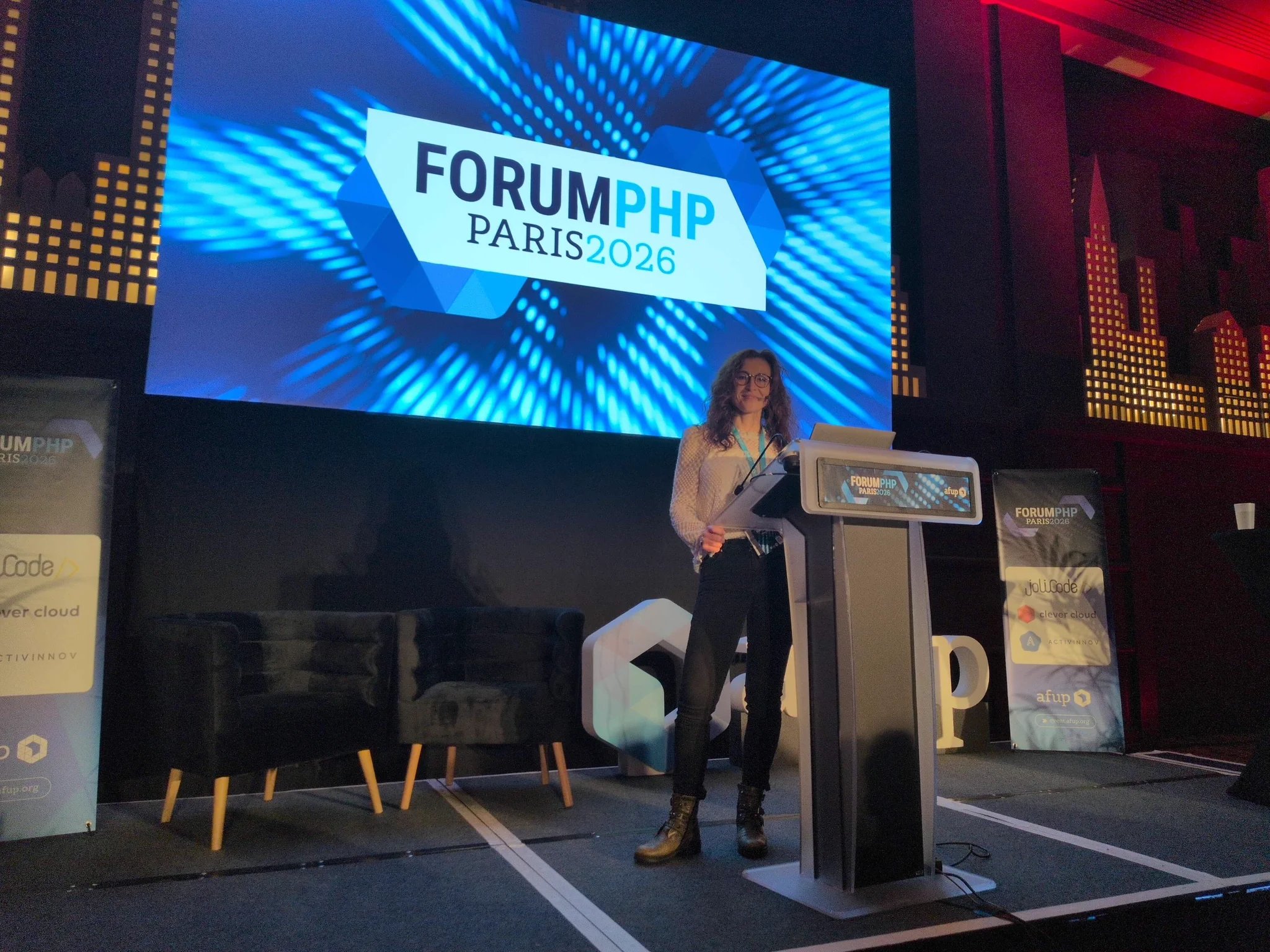 Marilena Ruffelaere debout sur scène derrière un pupitre et devant un grand écran affichant Forum PHP Paris 2026