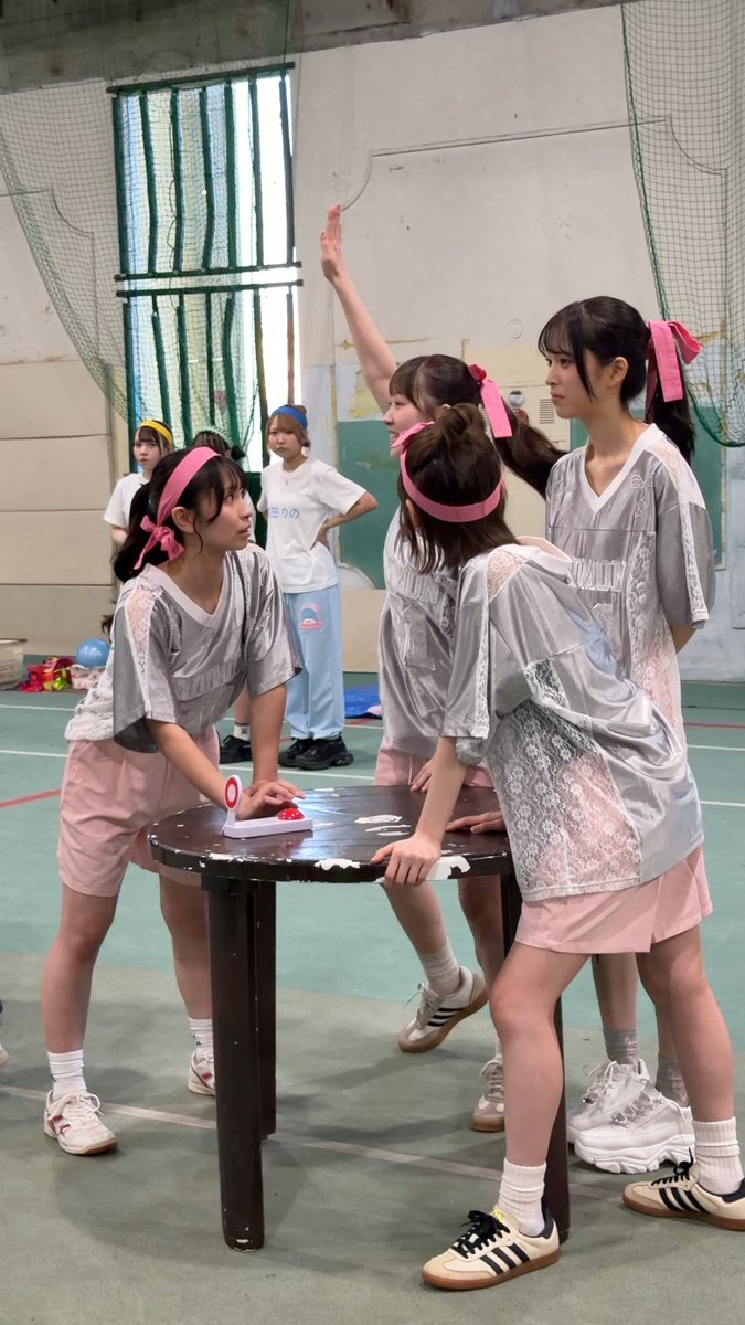 A group of young women wearing matching gray jerseys with "NATION" text and pink shorts or headbands gathered around a small table in what appears to be a gym.