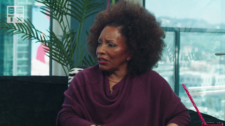 The image shows singer Stephanie Mills in an interview setting, wearing a deep purple sweater with a green plant visible behind her, as she discusses Chris Brown being "the closest thing to Michael Jackson." A red and white striped straw sits in a glass in the foreground, and the BET logo appears in the corner.
