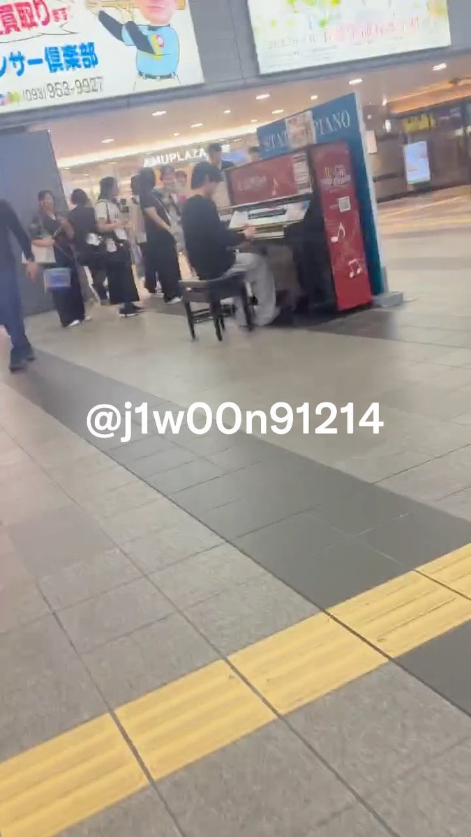 A street piano performance in a Japanese shopping plaza, watermarked '@j1w00n91214', with onlookers gathered around the player.