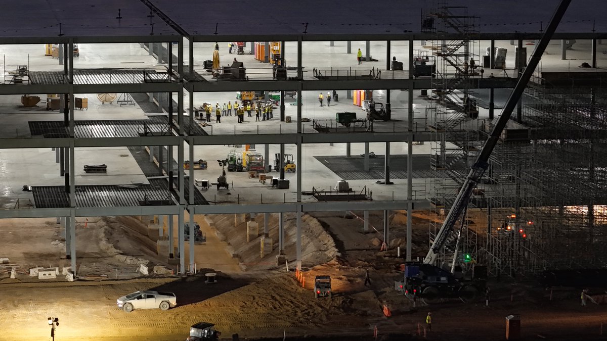 JoeTegtmeyer's tweet photo. The Optimus Factory at Giga Texas like you’ve never seen before! At night and all lit up showing off great views inside the structure that is now ~40% steel assembled! The main steel assembly may be complete by the end of the 1st Qtr in 2027, which would be truly amazing since that would be around 1 year after initial ground breaking began!

We can see the ground floor still has a lot of open trenches & part of the deep “plus” foundation footing pit still unfinished, along with some utilities work. The upper 3 floors show much has had concrete poured & even some sections os the roof as well ahead of the weatherproof membrane that will be installed once the roof is ready.

Take a look at the factory in a “new light’ today ! 😎🤖