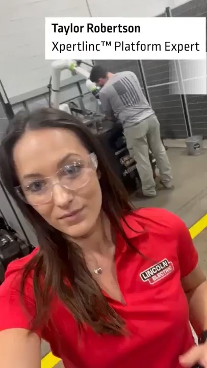 Selfie video of Taylor Robertson, labeled 'XpertLinc™ Platform Expert', wearing safety glasses and a red Lincoln Electric polo shirt in a workshop.