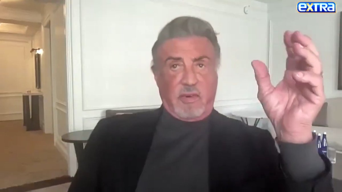 Sylvester Stallone appears on a video call in a black blazer and dark shirt, with an "EXTRA" logo visible in the corner.
