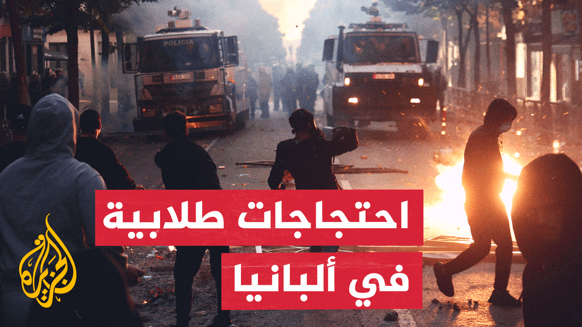 The image depicts a nighttime scene of civil unrest with silhouetted protesters facing police water cannon trucks marked "POLICIA," while flames burn on the street, conveying the intensity of the clashes. Arabic text overlaid on the image reads "احتجاجات طلابية في ألبانيا" (Student protests in Albania), with the Al Jazeera logo visible, and the accompanying post reports on clashes between Albanian police and university students protesting education conditions in Tirana.