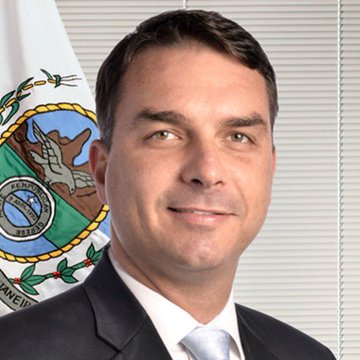 The image shows a professional portrait of Flávio Bolsonaro, a Brazilian politician and senator, wearing a dark suit and light blue tie, posed in front of the Brazilian flag. The caption relates to the post showing him as a leading candidate polling ahead of Lula in a hypothetical second-round election matchup.