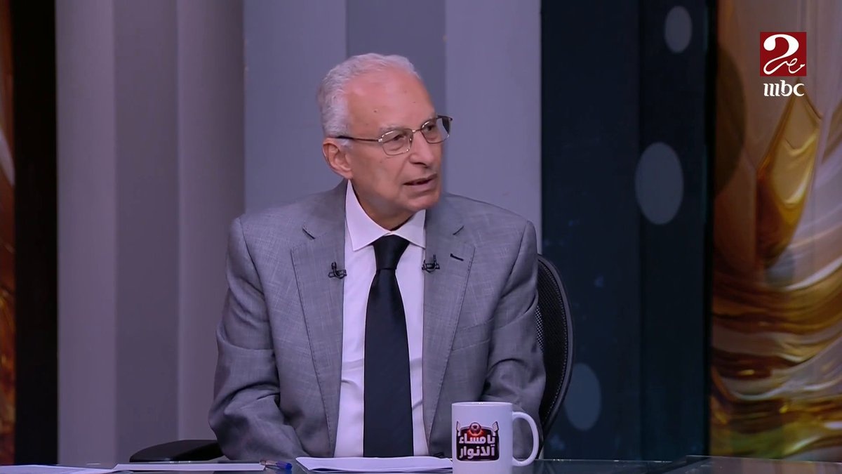 A television broadcast on 'mbc' features an older man with white hair and glasses in a gray suit, sitting at a desk with an Arabic news program logo.