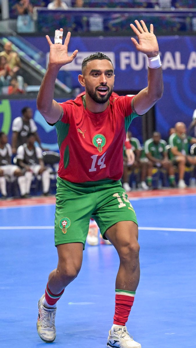 A futsal player wearing Morocco's #14 jersey celebrates with both arms raised in triumph on the court, with "#14" visible on his red and green uniform and a "FUTSAL" banner in the background, perfectly matching the excitement of securing a spot in the #TotalEnergiesAFCONFutsal2026 semi-finals.