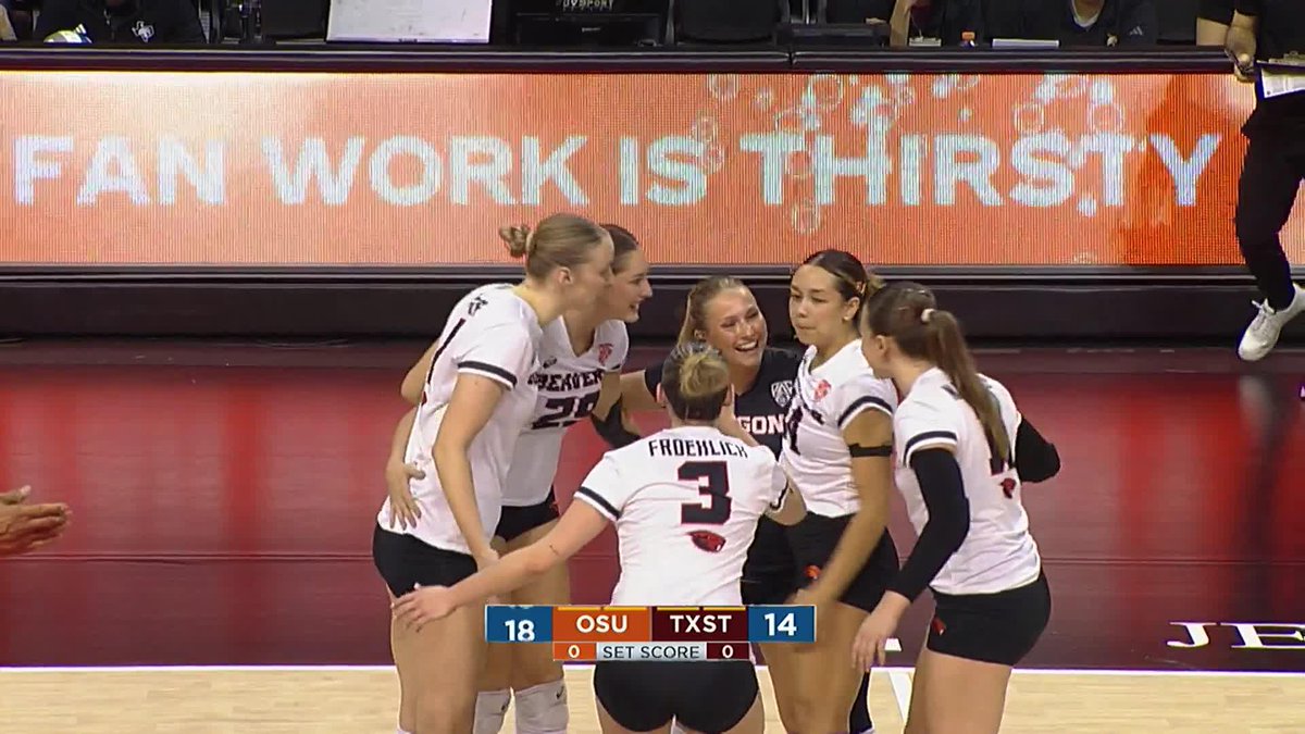 Oregon State volleyball players huddle together during a match against Texas State, with the scoreboard showing OSU leading 18-14 in the first set.