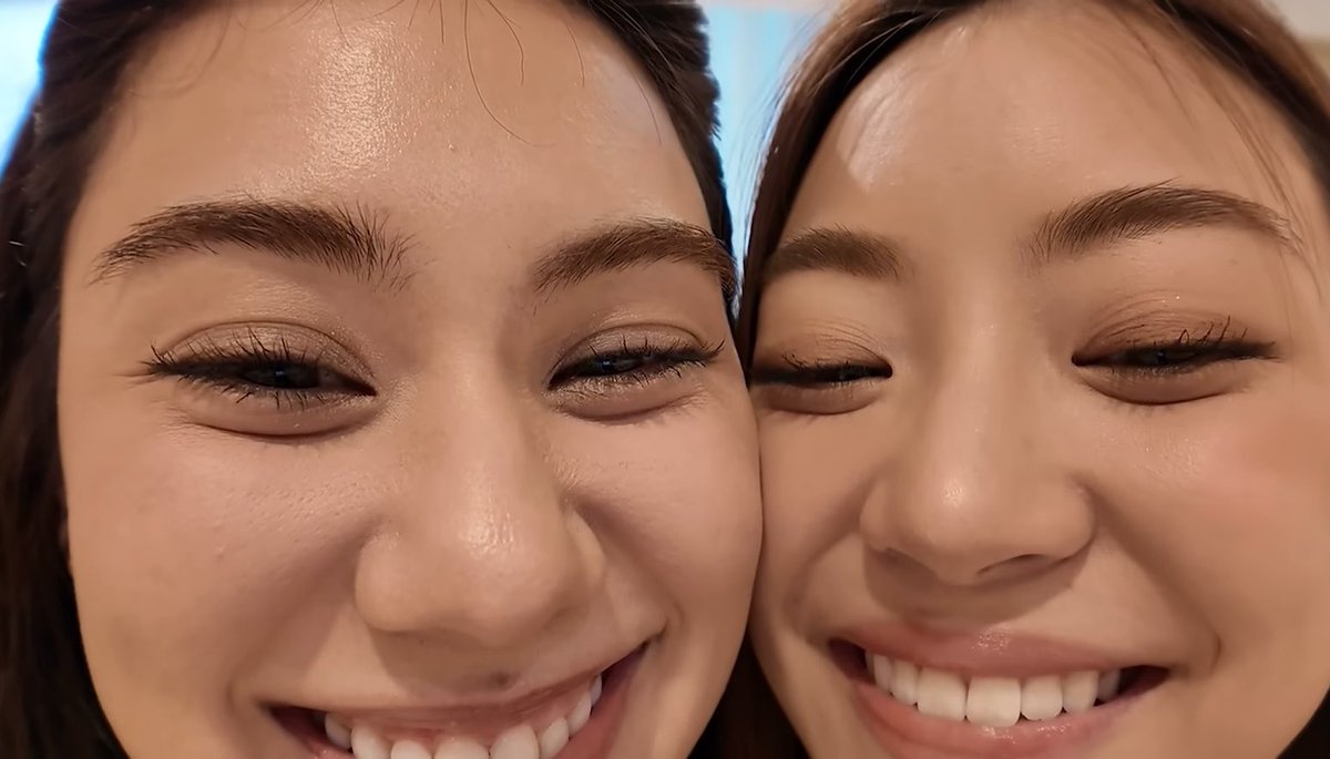 A close-up selfie of two young women smiling brightly, showing their eyes and smiles in detail.