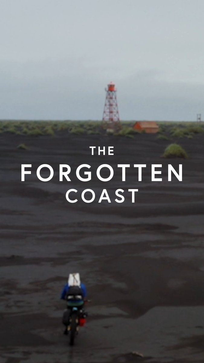 A lone cyclist with loaded gear rides across a dark volcanic landscape toward a red and white lighthouse, with overlaid text reading "THE FORGOTTEN COAST."
