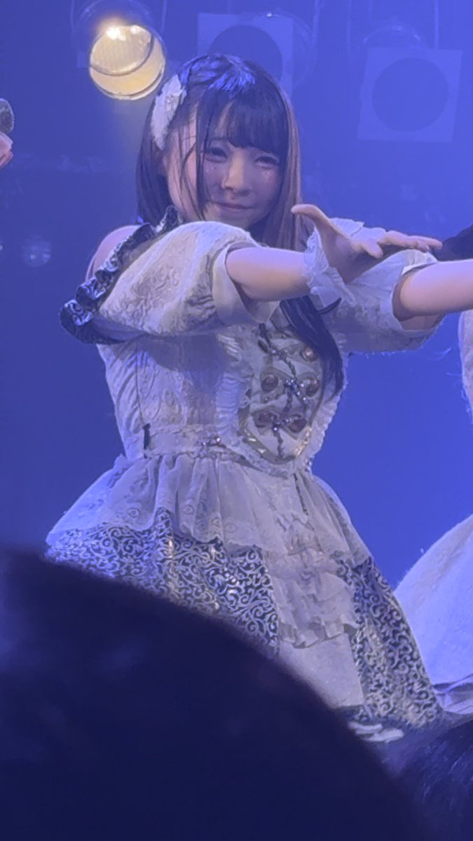 A Japanese woman performing on stage in an elaborate white and gold frilly dress with lace details, under what looks like idol concert lighting.