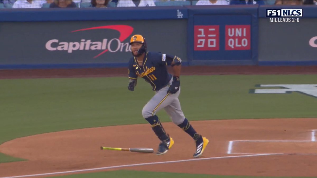 A Milwaukee Brewers player wearing number 11 sprints away from home plate after dropping his bat, with the FS1 NLCS broadcast showing "MIL LEADS 2-0" and a Capital One advertisement visible on the outfield wall. The image captures the moment Jackson Chourio hits the ground running to score for the Brewers in Game 3 of the NLCS against the Dodgers.
