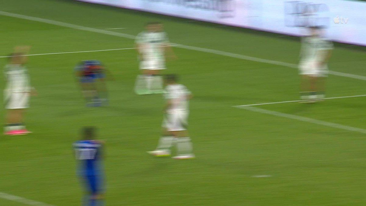 Soccer players in white and blue uniforms run across a green field in a blurred action shot, with a "v tv" logo visible in the upper right corner. The image captures the dynamic moment following Kevin Denkey's goal that narrowed FC Cincinnati's deficit to one goal.