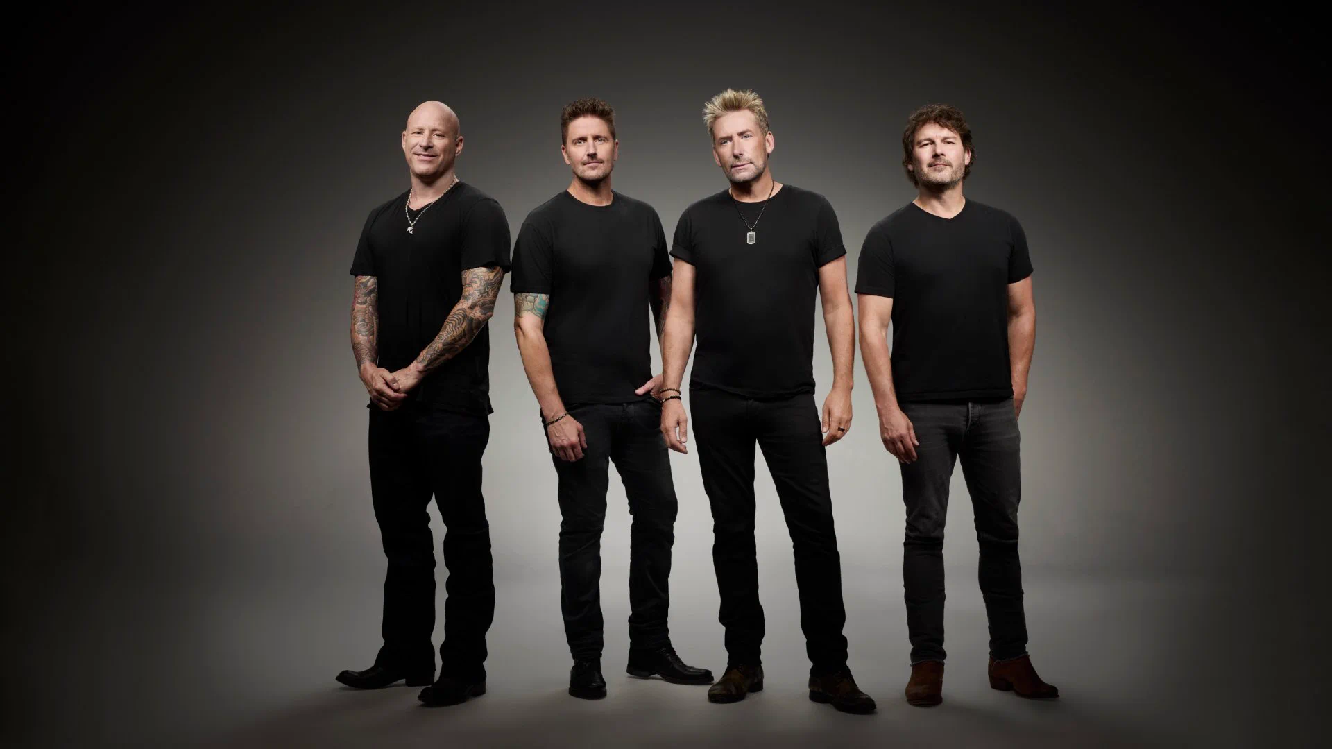The four members of Nickelback pose together against a gray studio backdrop, wearing black T-shirts and dark pants.
