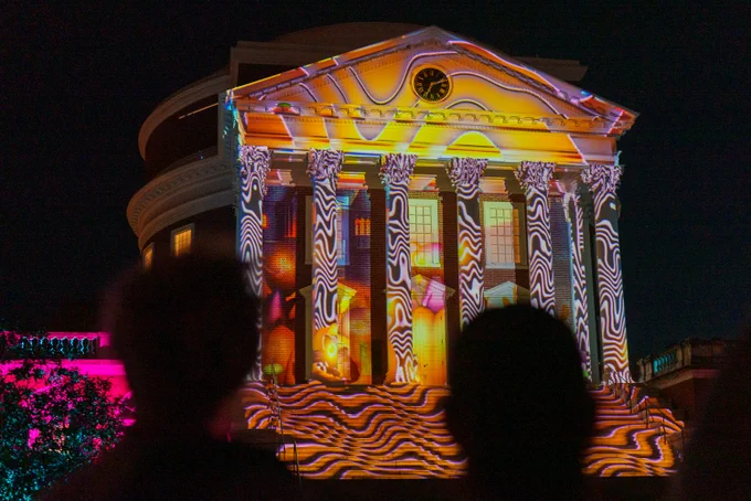The University of Virginia’s Rotunda illuminated with colorful, abstract light projections during The Great Rotumpkin. Silhouettes of onlookers are visible in the foreground.