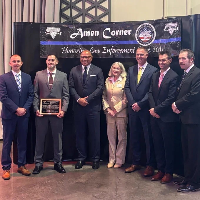 Seven people stand in front of backdrop reading "Amen Corner: Honoring Law enforcement." One man holds a plaque.