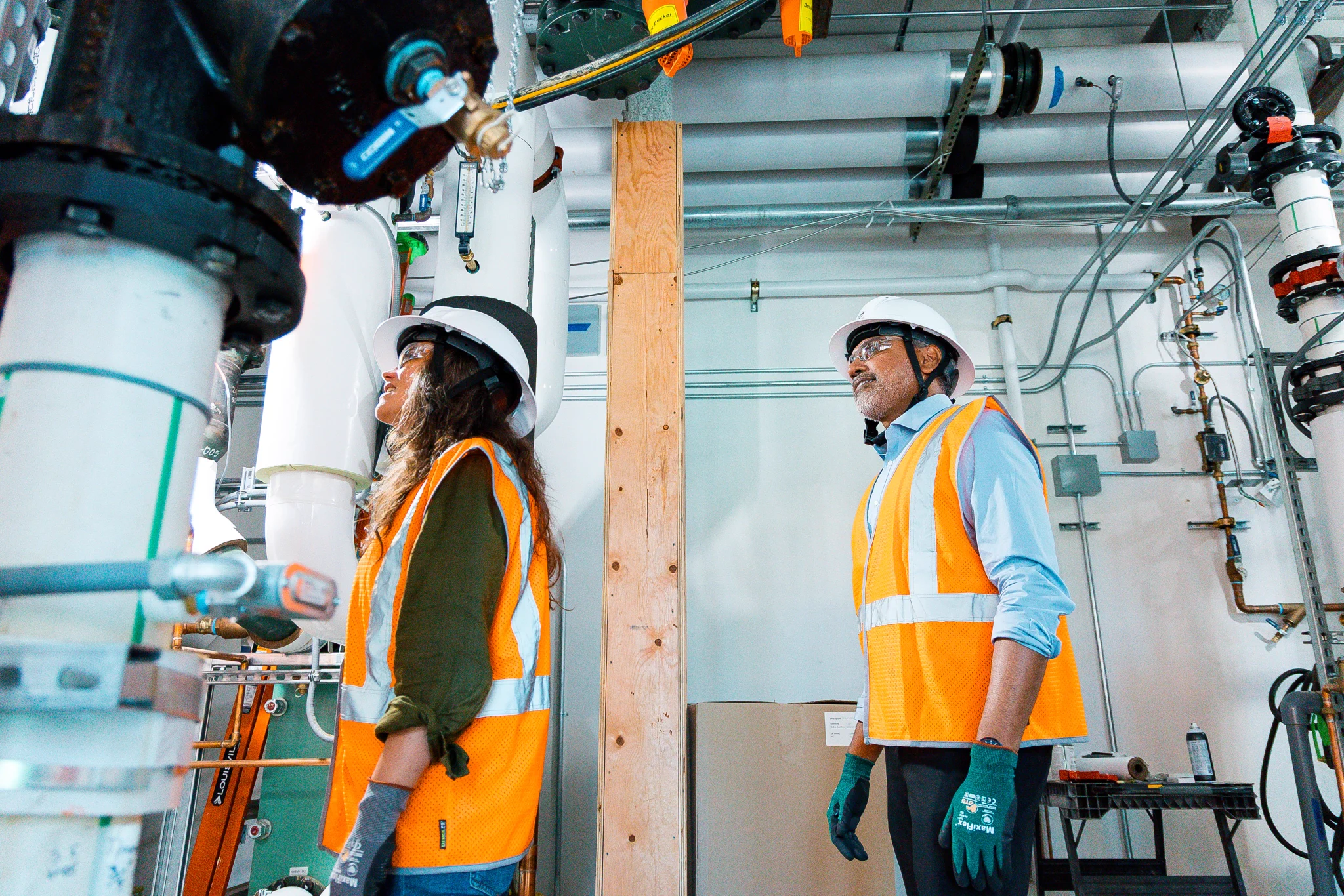 Two individuals in safety vests and other PPE look up inside of a building under construction.