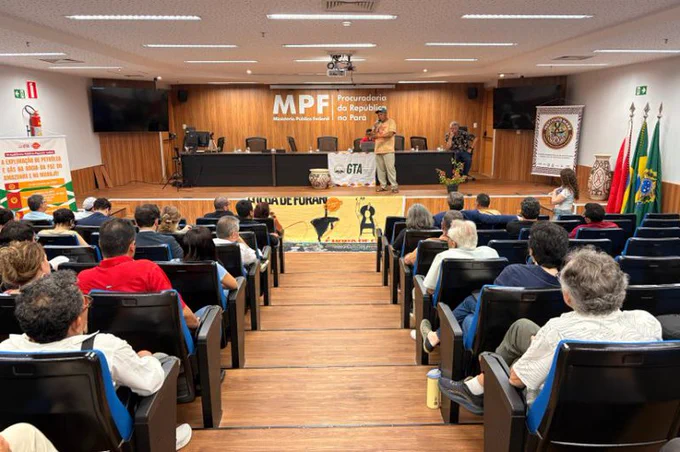 Auditório com público sentado assistindo a um homem falar ao microfone no palco, sob a sigla MPF em parede de madeira ao fundo. Foto: Yasmim Bitar/Comunicação MPF.