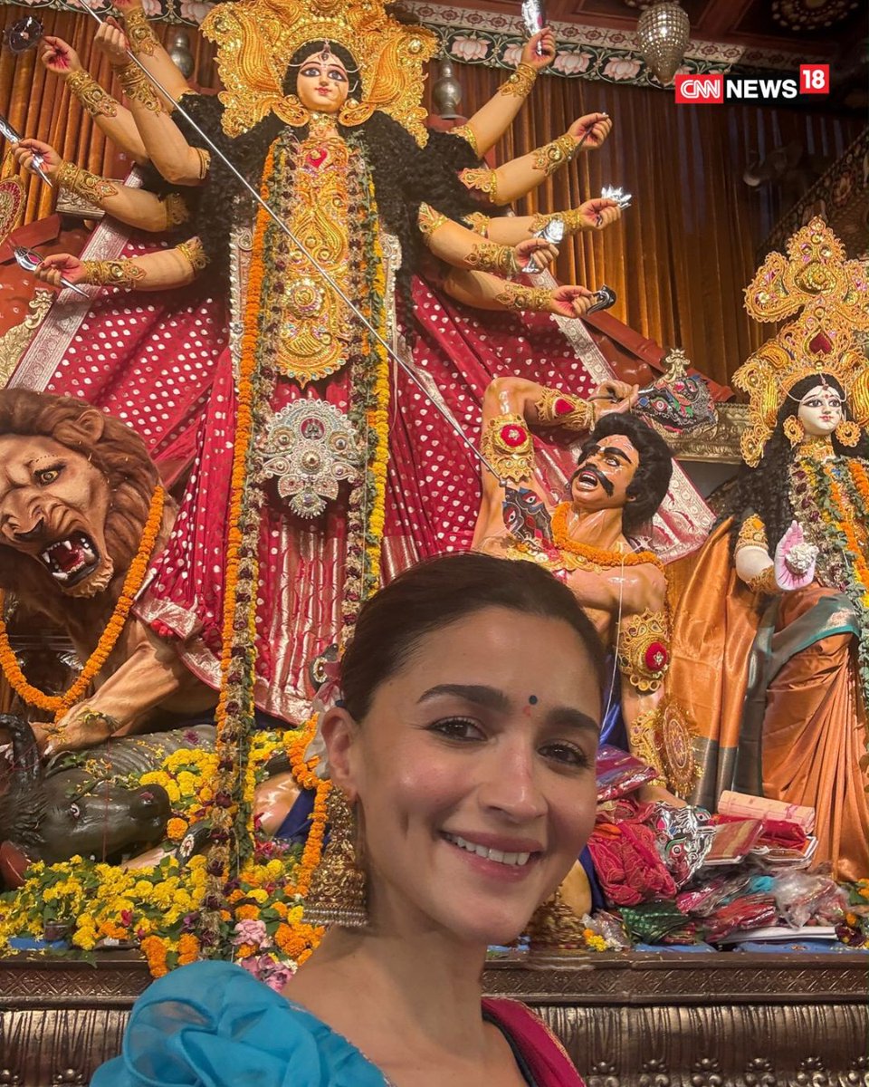 CNNnews18's tweet photo. Bollywood star Alia Bhatt attended the North Bombay Sarbojanin Durga Puja, organised by the family of her close friend and director Ayan Mukerji. The actor channelled her Rocky Aur Rani Kii Prem Kahaani character Rani Chatterjee in a red saree paired with a sky-blue puff-sleeved blouse featuring lotus and crescent moon motifs. 

She completed her festive look with a neat bun adorned with a gajra, gold jhumkas, bangles and a cocktail ring. Alia also participated in the aarti and served bhog at the pandal. Her visit came days after her husband, actor Ranbir Kapoor, who stars in Ramayana, attended the Durga Puja celebrations.

#AliaBhatt #Bollywood #DurgaPuja