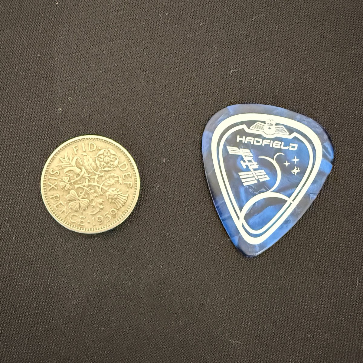 Cmdr_Hadfield's tweet photo. Great fun trading used guitar picks with Brian May of Queen. 
He uses old sixpences, and was kind enough to find one with my birthyear at our concert this weekend. I use hard plastic ones, the mission emblem from my 3rd spaceflight. 
(such a fine person, Sir Brian May, PhD astrophysicist & phenomenal musician/human, @DrBrianMay of @QueenWillRock)
