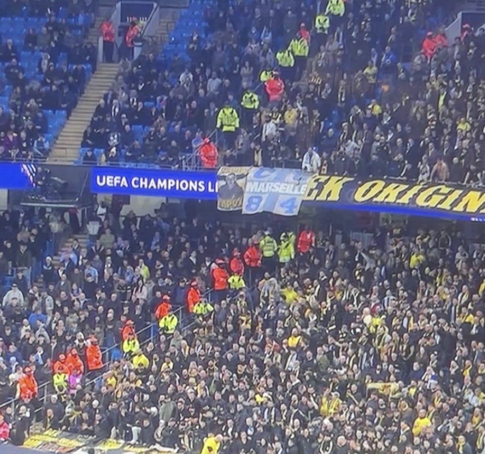 InformaTreize's tweet photo. Les supporters de l’AEK sortent un drapeau des CU84 face à Manchester City ! 

👉 🟡⚫️ 𝘅 🔵⚪️ ! #TeamOM https://t.co/0UJUdLbu8d