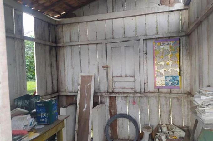 Interior de estrutura de escola, formada por madeira clara com uma pequena janela de madeira fechada, cartaz colorido, latas de tinta e objetos empilhados. Foto: Funai, 2022.