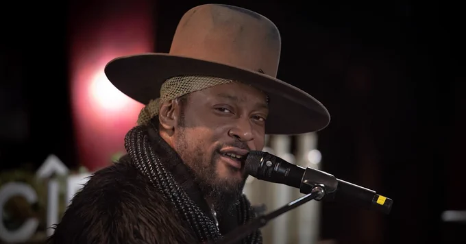 D'Angelo in a wide-brim hat singing into a microphone