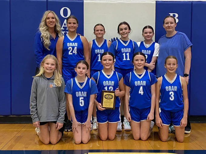 Oran girls basketball team poses with two coaches in a gym, wearing blue uniforms and holding a second-place tournament plaque.