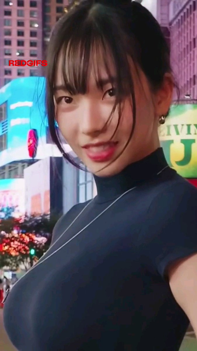 A woman with bangs in a black sleeveless turtleneck poses in what appears to be Times Square, with a 'REDGIFS' watermark in the upper left corner.