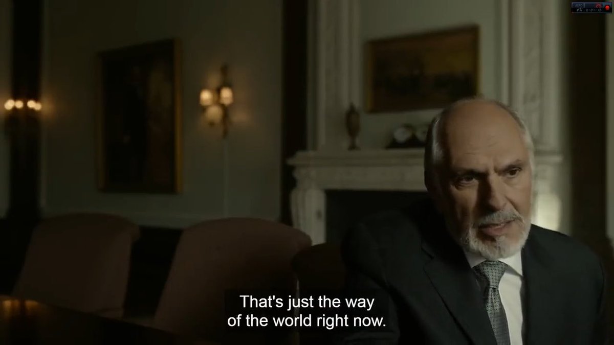 A dim interior scene shows an older bald man with a white beard seated in a suit; the subtitle reads, “That’s just the way of the world right now.”